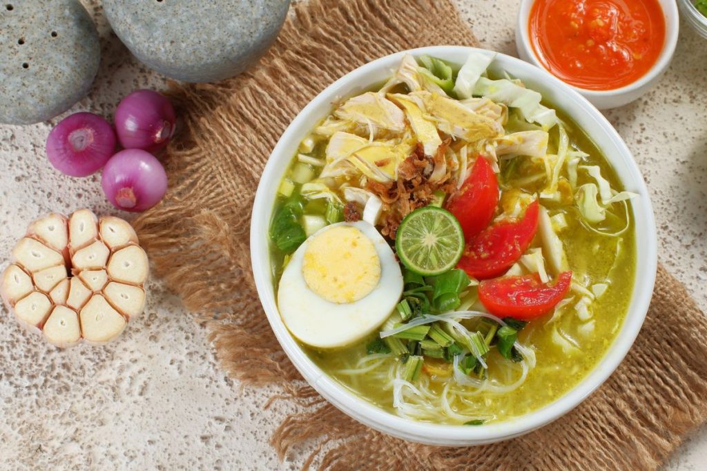 Semangkuk soto daging kuah bening dengan irisan daging sapi, tauge, daun bawang, seledri, bawang goreng, dan jeruk nipis siap disajikan.